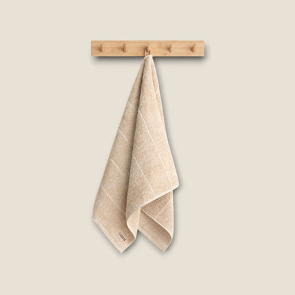 Madhome.ro beige cotton bath towel hanging on a wooden hook, featuring a soft, absorbent, and textured design.