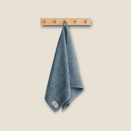 Madhome.ro blue cotton bathroom towel hanging on a wooden wall hook, featuring a soft, absorbent texture.