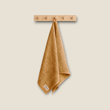 Madhome.ro soft brown cotton bath towel hanging on a wooden wall hook, featuring a dense 600 gsm texture.