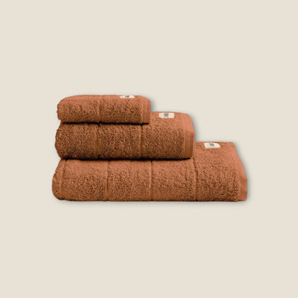 Madhome.ro set of three soft brown cotton bath towels stacked neatly, featuring a dense texture and elegant hem.