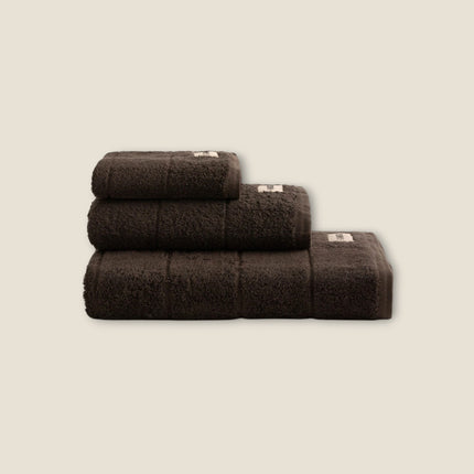 Madhome.ro set of three dark brown fluffy cotton bath towels stacked neatly on a neutral background