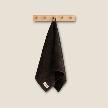 Madhome.ro dark brown cotton bath towel hanging on a wooden wall hook, featuring a soft and absorbent texture.