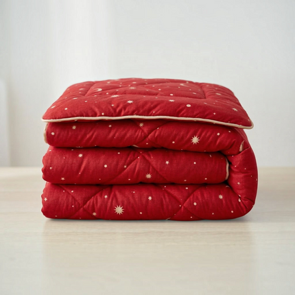 Madhome.ro red quilted spring duvet with a star and moon pattern folded neatly on a light wooden surface