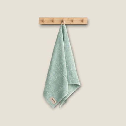 Madhome.ro soft sage green cotton bath towel hanging on a wooden hook, featuring a dense and absorbent texture.